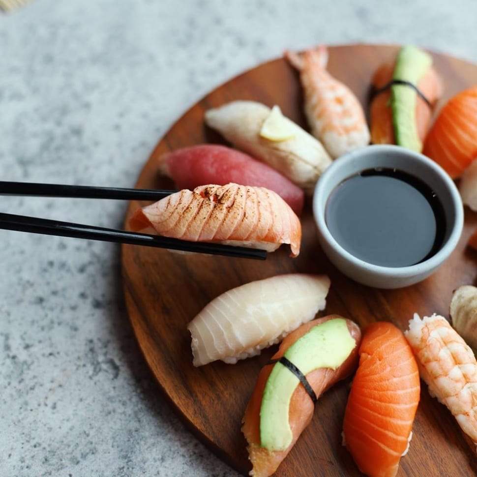 Variety of salmon, tuna, tilapia nigiri on round wooden board