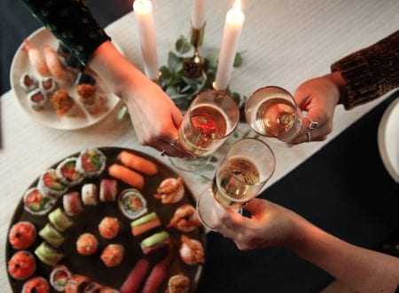 Celebration of friends around a table with sushi, candles and glass of wine.