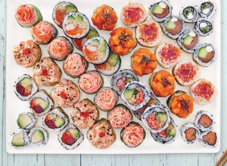 Family platter of various sushis on white plate and light blue wood table