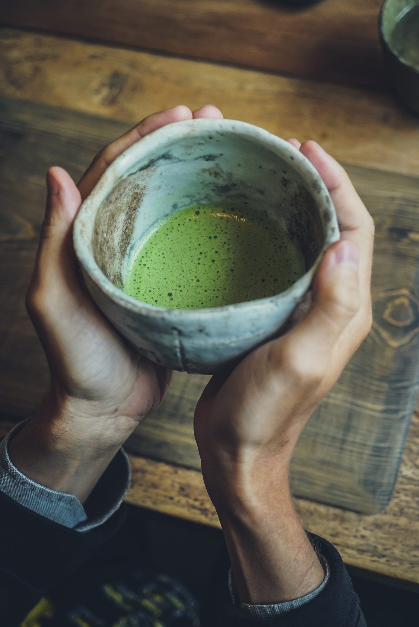 Hands hold ceramic cup with green tea
